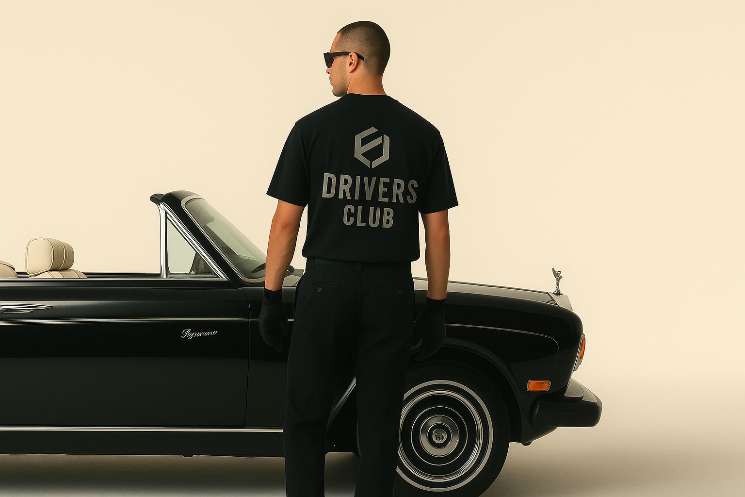 Person wearing a 'Drivers Club' t-shirt standing next to a black car on a beige background